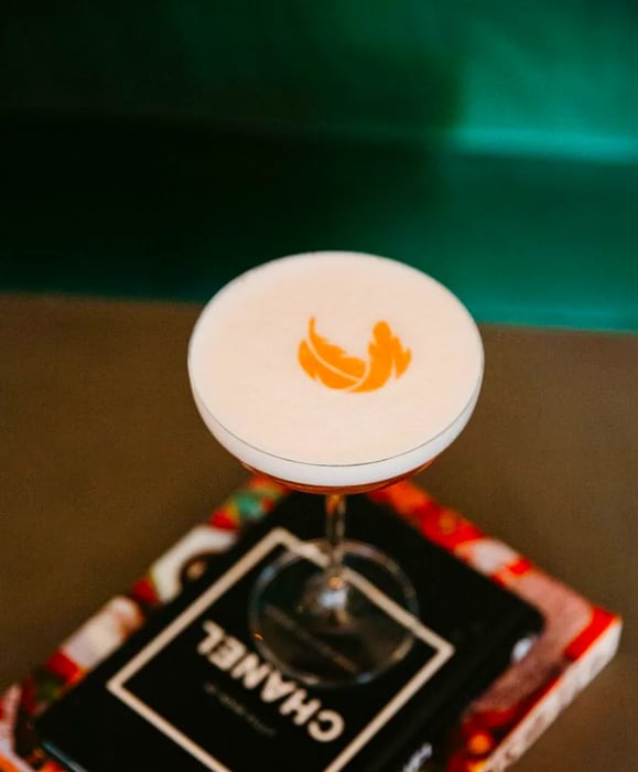 A cocktail topped with foam art shaped like a leaf.