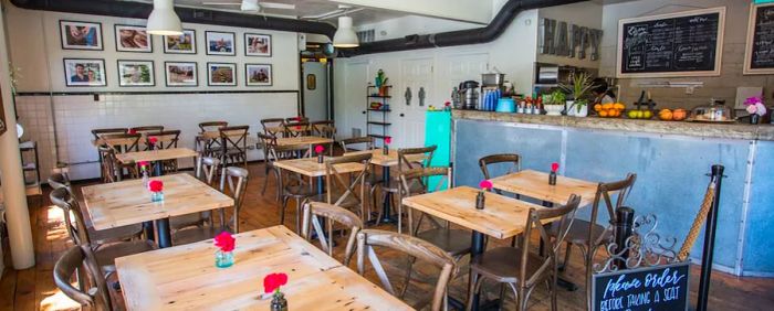 The cafe's interior features empty tables, a counter filled with baskets of fruit, chalkboard menus, and framed photographs adorning the walls.