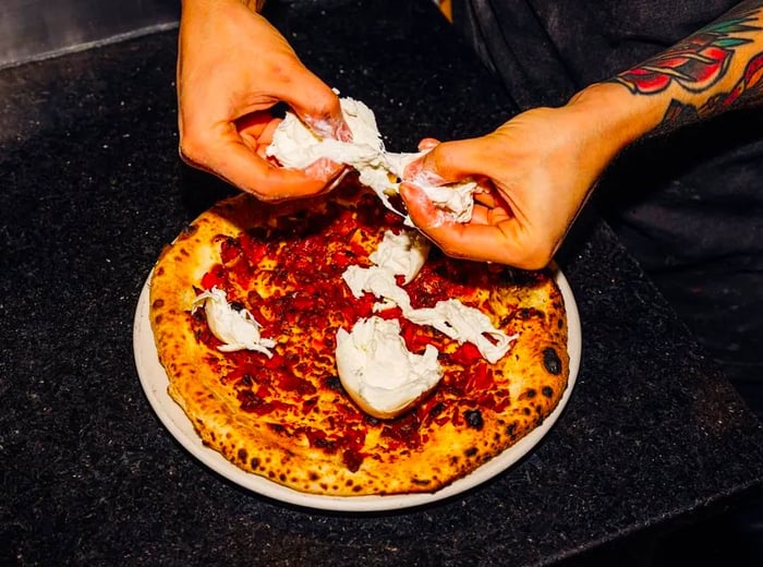 A chef shreds cheese to sprinkle on top of a pizza.