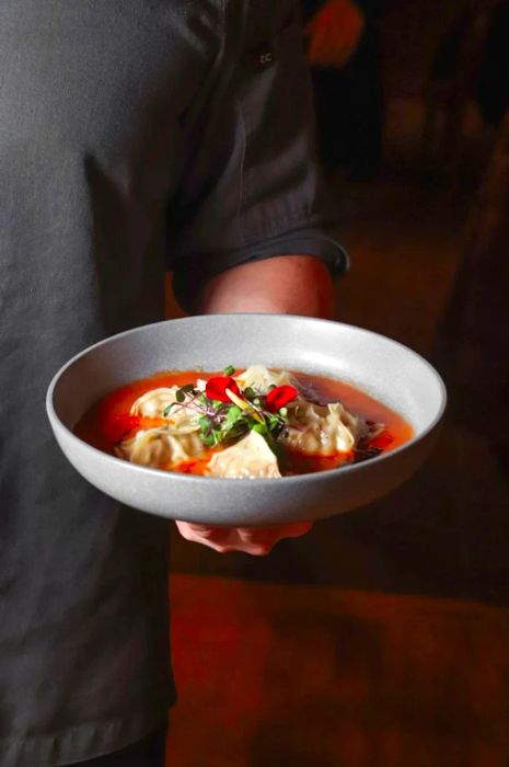 A server presents a bowl of dumplings in vibrant red broth.