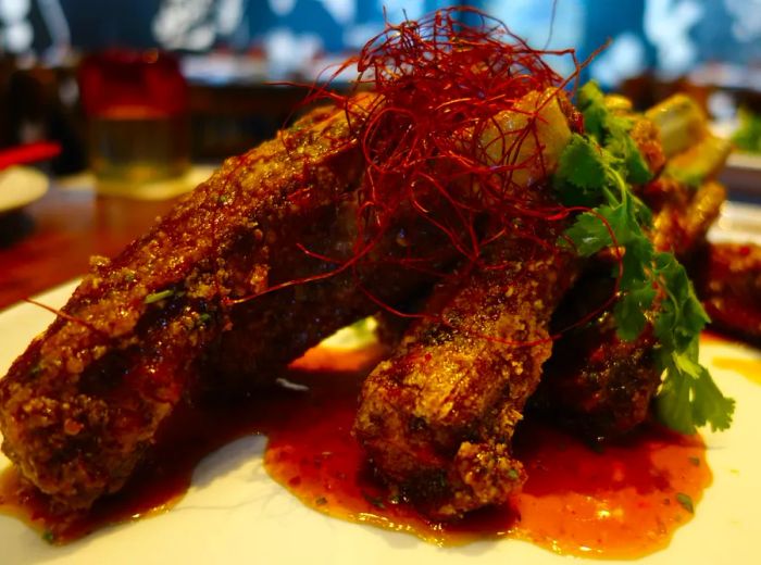 A generous stack of spare ribs resting on a plate with a drizzle of sauce.