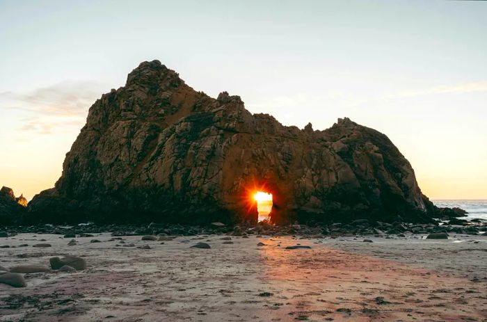 Sunset light filters through the arch of a rock formation at Pfeiffer Beach, Big Sur, California