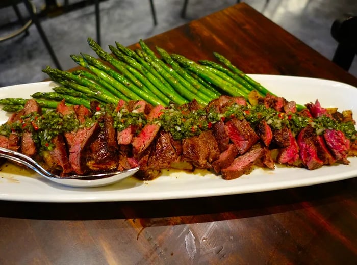 A generous slice of skirt steak drizzled with chimichurri, accompanied by green beans.