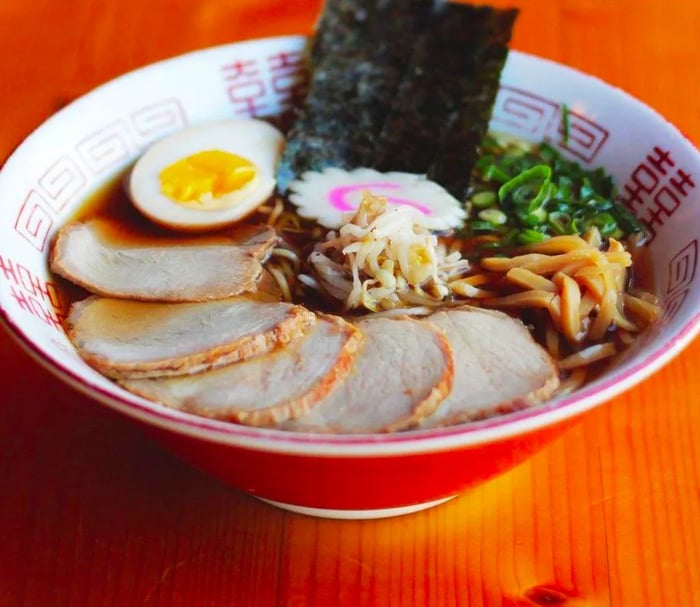 A steaming bowl of ramen adorned with tender slices of meat, a soft-boiled egg, fresh vegetables, and seaweed.