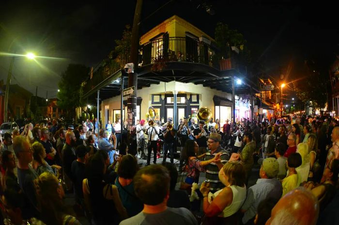 A local brass band performs on a street corner on Frenchmen Street at night, surrounded by an enthusiastic crowd.