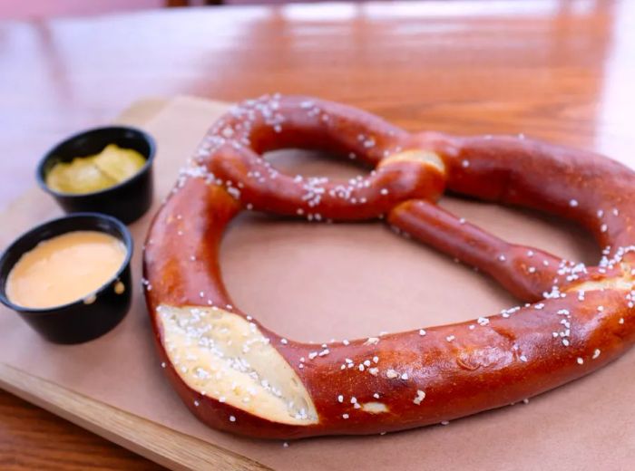 A hefty pretzel presented on butcher paper alongside a variety of dipping sauces.