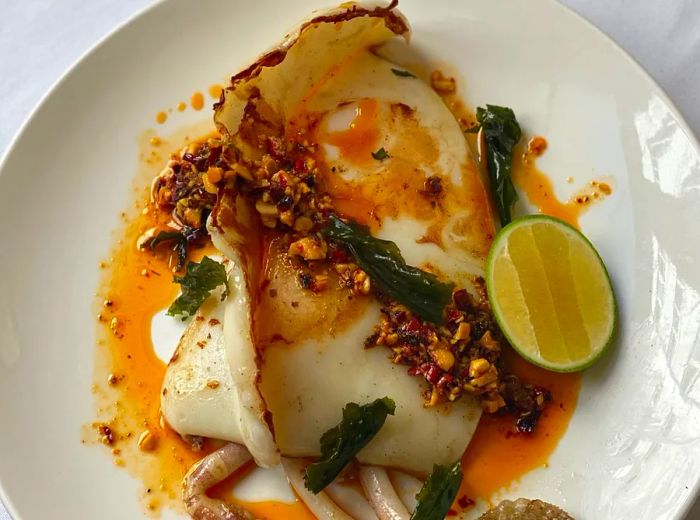 Aerial view of a fish dish adorned with chili crisp, fresh greens, and a lime wedge.