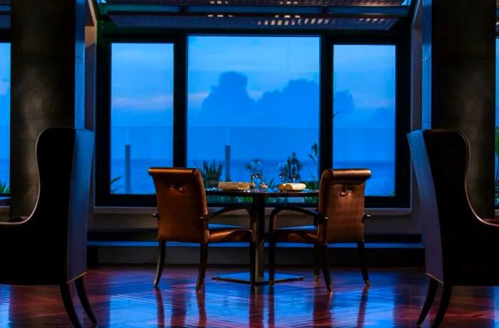 A vacant table in a dining area, gazing out at a darkened sky and ocean beyond.