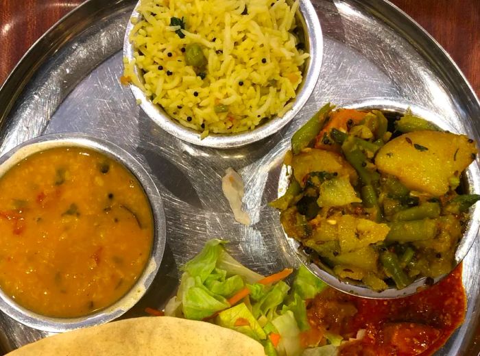 A thali featuring rice, vegetables, and curry accompanied by a large piece of flatbread.