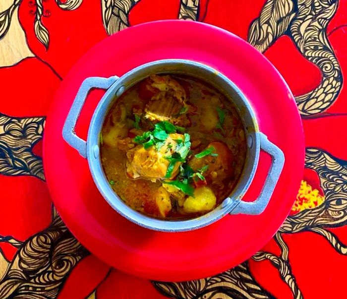 A top view of a metal bowl of soup resting on a plate, set against a vibrant red tablecloth.