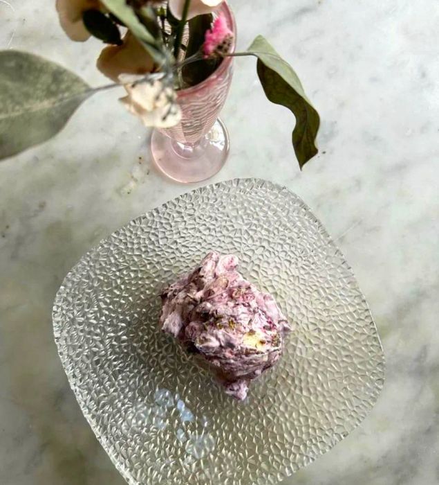 A light, fluffy purple meringue presented on a glass dish, accompanied by a vase of flowers.