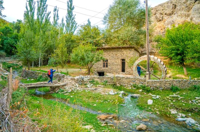 Uzbekistan, a woman hiking in the Nuratau mountains near Asrof, beside a watermill.