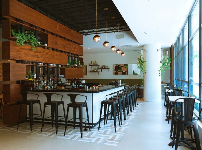 A chic dining area filled with natural light, featuring cement flooring, pendant lights above the bar, and an elegant wooden back bar.