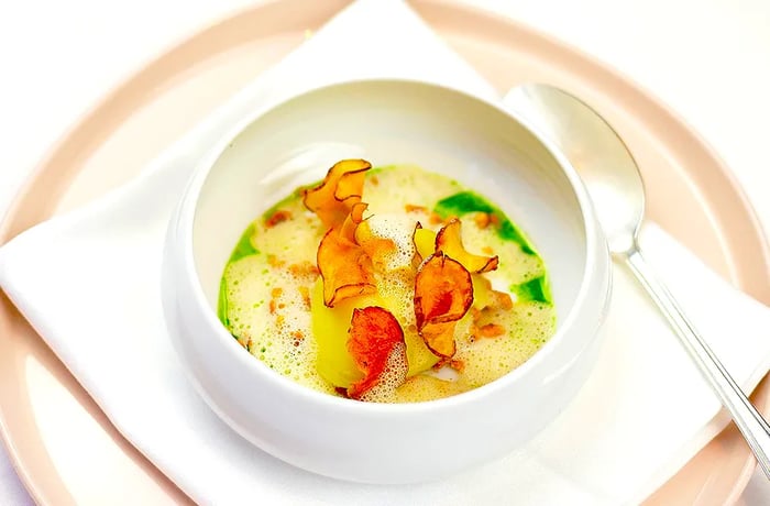 A frothy bisque featuring slices of root vegetables protruding from it.