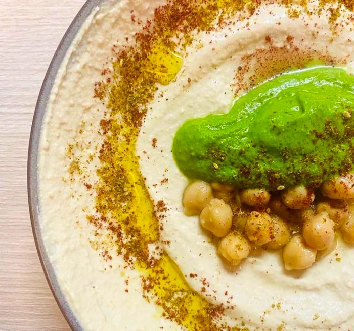 A close-up of hummus topped with half an avocado, chickpeas, and a drizzle of oil.