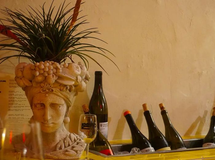 Wine bottles nestled in a hidden ice bucket against a wall, with a Frida Kahlo bust repurposed as a planter nearby.