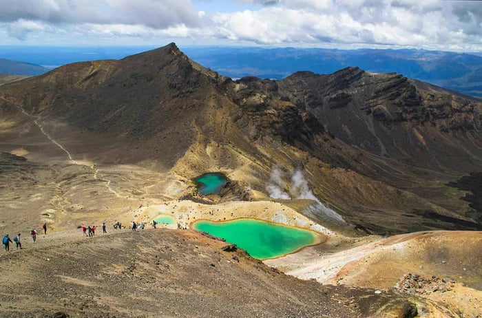 Hikers traverse volcanic terrains and lush lakes on the Tongariro Alpine Crossing in New Zealand