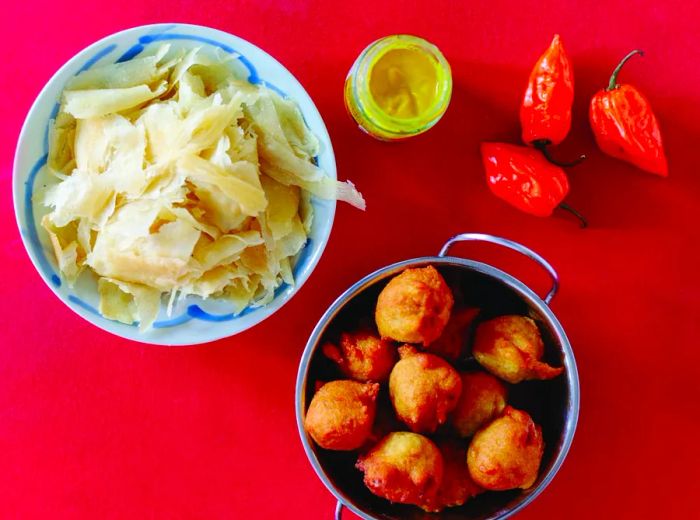 Bowls of pholourie and buss up shut, placed alongside vibrant red peppers.