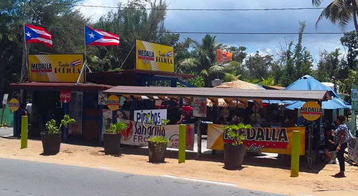 An open-air eatery featuring outdoor seating adorned with advertisements and fluttering Puerto Rican flags.