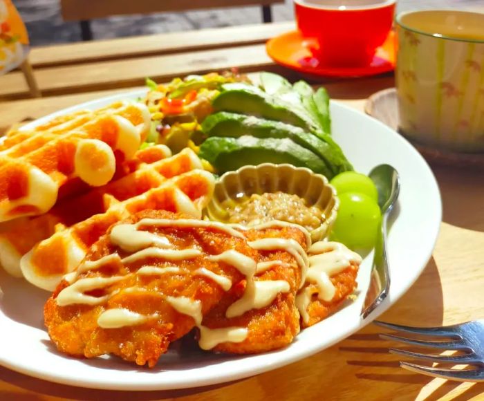 A delightful mixed plate featuring waffles, avocado, and other tasty items on a sunlit patio table.