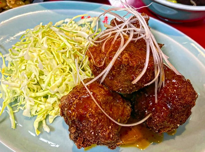 Three glossy pieces of fried vegan karaage presented with shredded cabbage and sides.