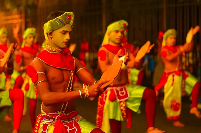 A group of male dancers, adorned in vibrant costumes and makeup, perform in unison, rhythmically clapping their hands against wooden paddles.