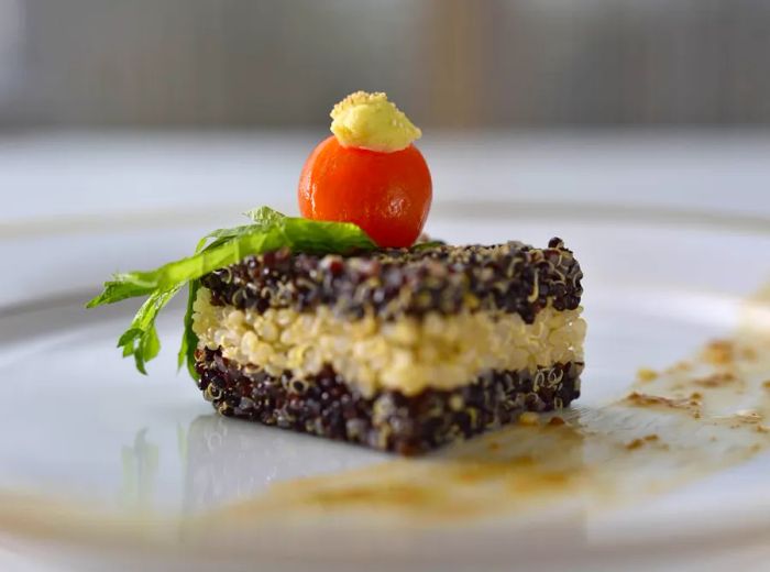 A layered dish resembling a sandwich, featuring contrasting black and white grains topped with a small orange sphere.