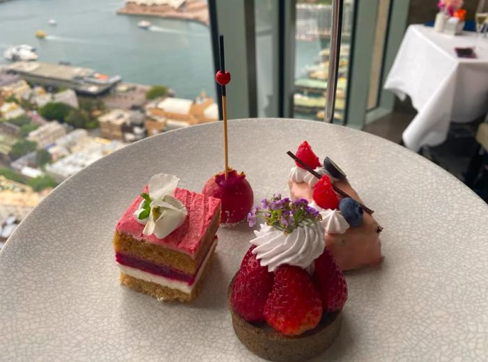 Four delightful pastries arranged on a plate, with a breathtaking view of Sydney visible through the window.