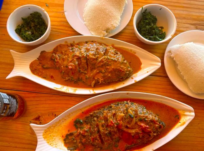 Two whole fish in a savory brown gravy, accompanied by sides of ugali and cooked spinach.