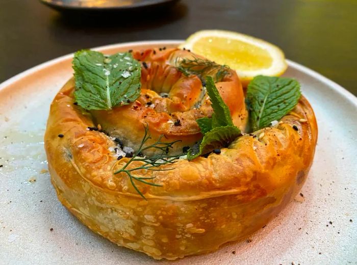 A round spanakopita served with fresh herbs and a lemon wedge.