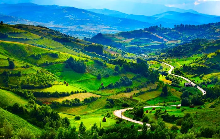 A picturesque view of a road meandering through a lush green valley in Transylvania.