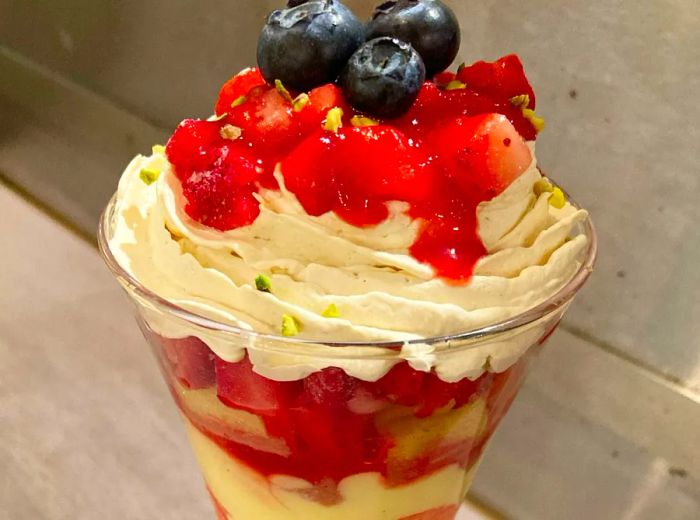 A tall glass parfait layered with fruit, topped with whipped cream and berries.