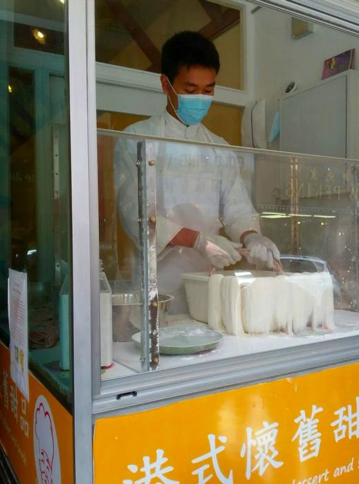 A chef pulls dragon’s beard candy from a vat in a glass-enclosed stall.