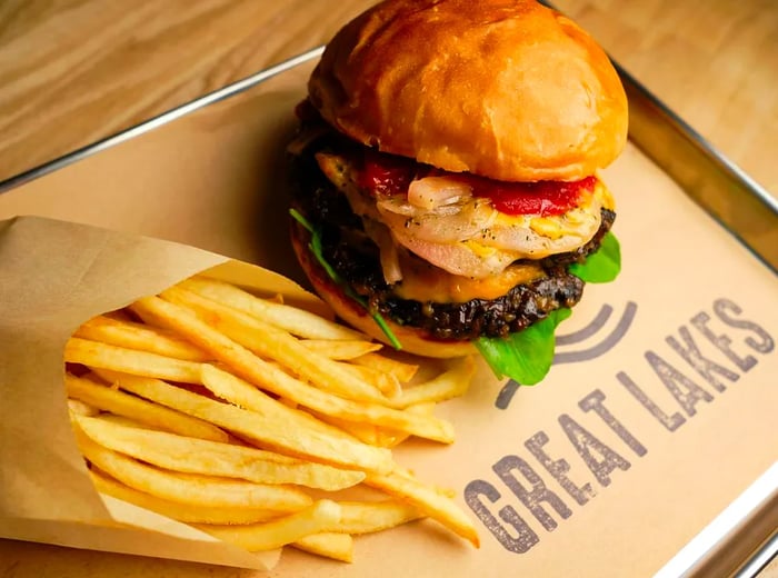 A veggie burger with French fries served on a metal tray lined with branded wax paper.