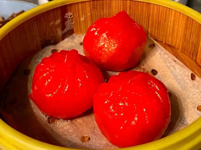 Three vibrant orange dumplings presented in a steamer basket.