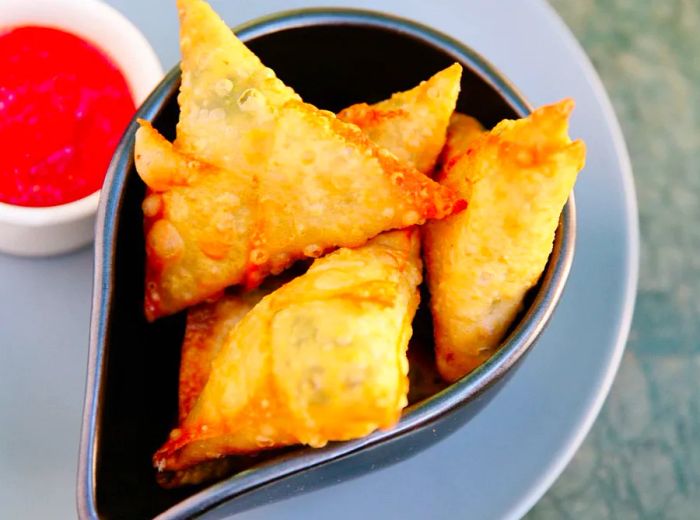 A plate of fried samosas, elegantly served with a red dipping sauce.