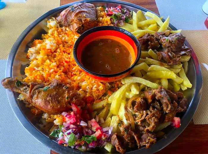 A generous platter featuring meats, fries, and rice, surrounded by a flavorful sauce.