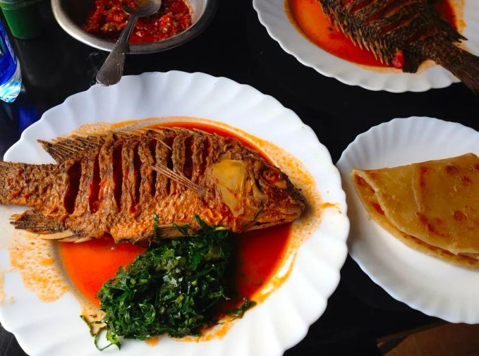 A whole fish served fried alongside greens and flatbread.