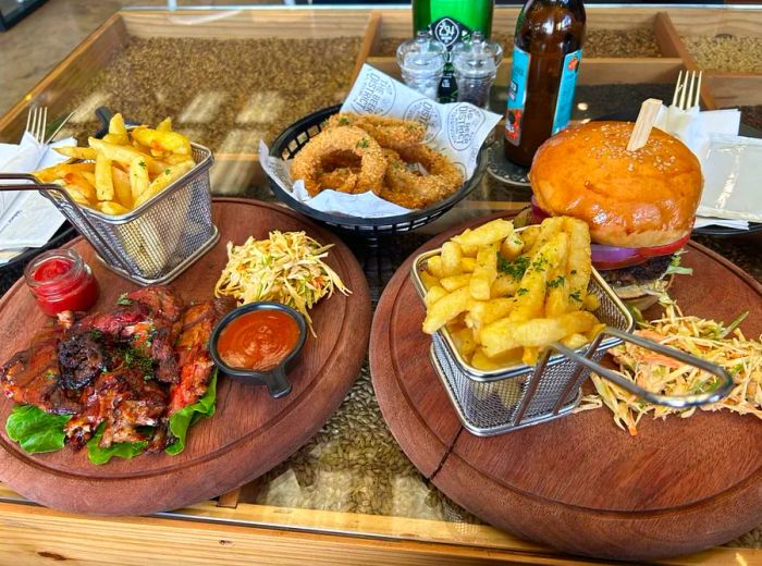 A burger paired with ribs, both served alongside French fries and a basket of crispy onion rings.