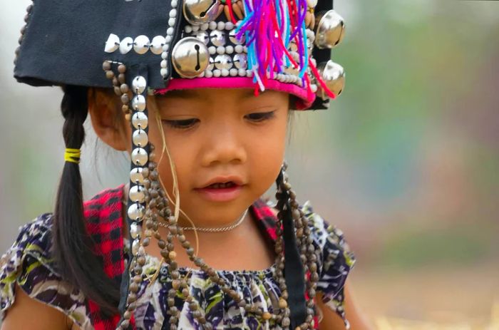 An Akha girl dons a headdress adorned with metal discs and vibrant threads.