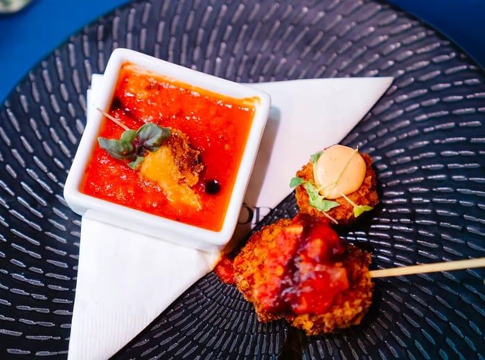 A fried skewer accompanied by a dipping sauce, elegantly arranged on a textured plate.