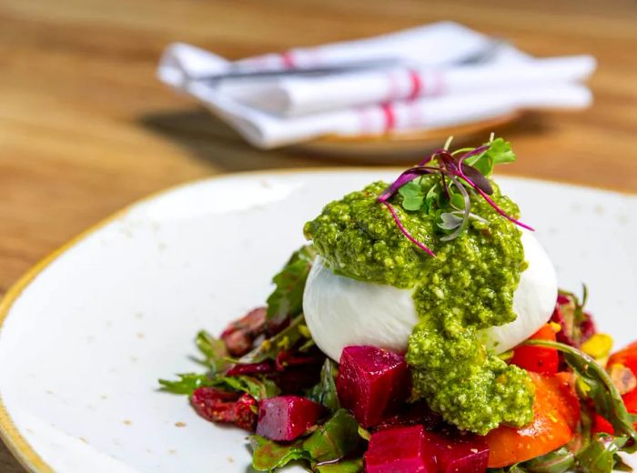 A round of burrata drizzled with pesto, resting on a bed of beets and tomatoes.