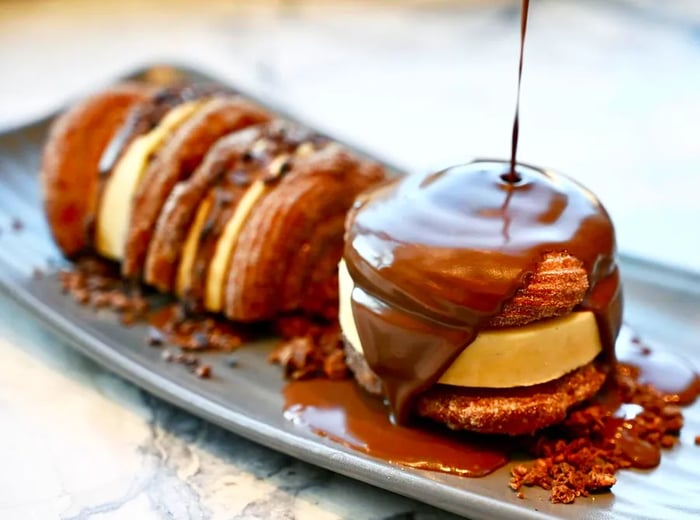 Chocolate drizzles over a dessert sandwich made with churros as buns.