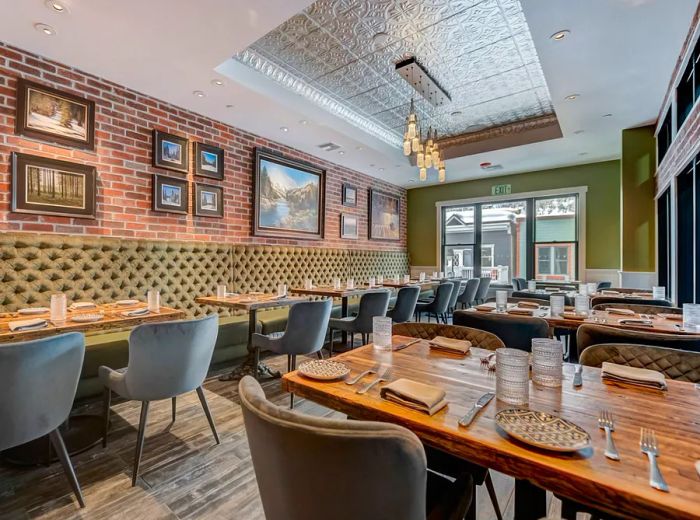 An elongated dining area with large windows at the far end, pendant lights suspended in the center, and tables elegantly set for dinner.