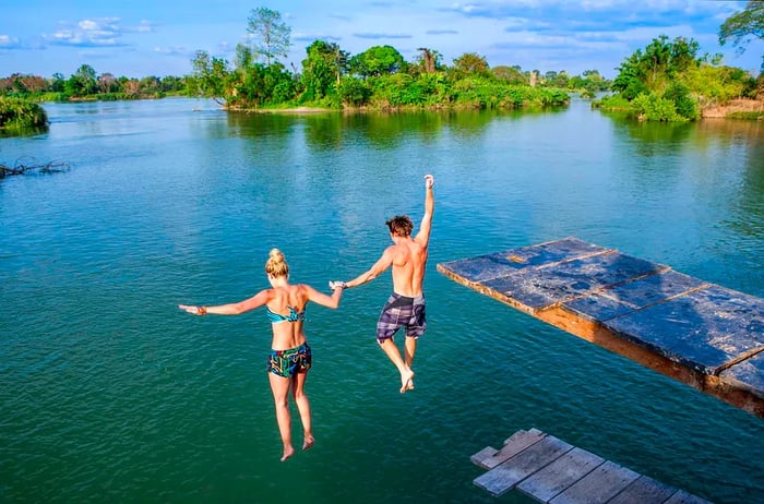 Two individuals leap off a platform into the Mekong River from Don Det Island, Laos.