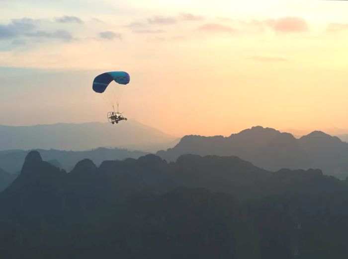 Tourists paramotoring over the dawn-lit valley in Vang Vieng, Laos