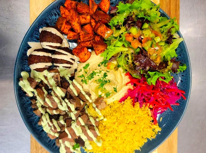 A bowl filled with falafel and fresh vegetables, drizzled with tahini.