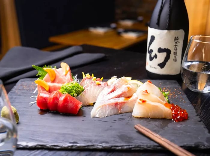 Sashimi slices artfully arranged on a slate board alongside sake.