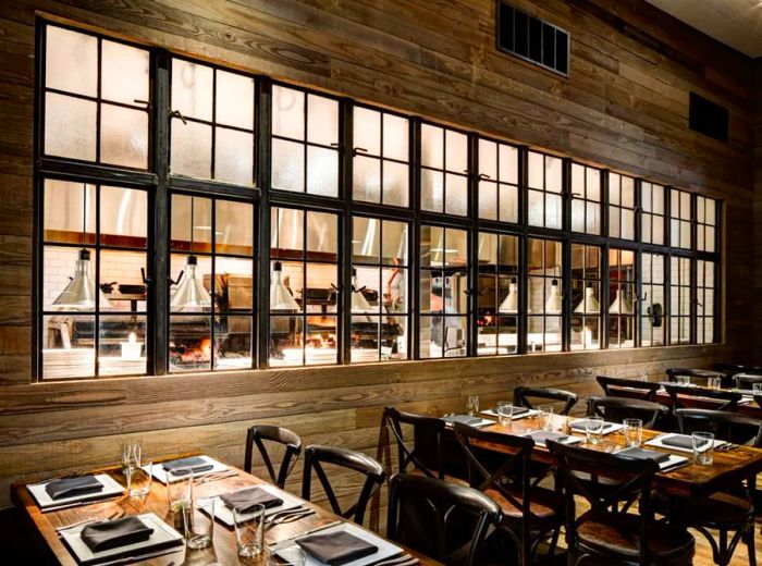 A row of large antique windows adorns one wall of the dining area, offering a view into the bustling kitchen.