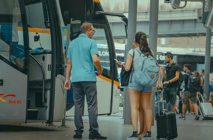 A bus driver converses with two passengers as they wait to board a coach at a bus station in Barcelona, Spain.